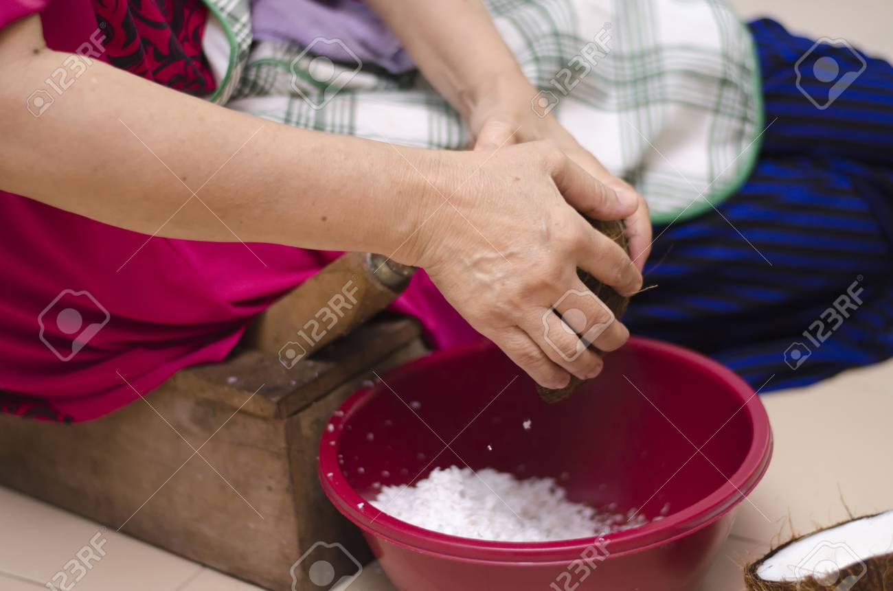 82165572-traditional-way-housewife-sit-on-wooden-coconut-grater-and-grate-coconut-into-container.jpg